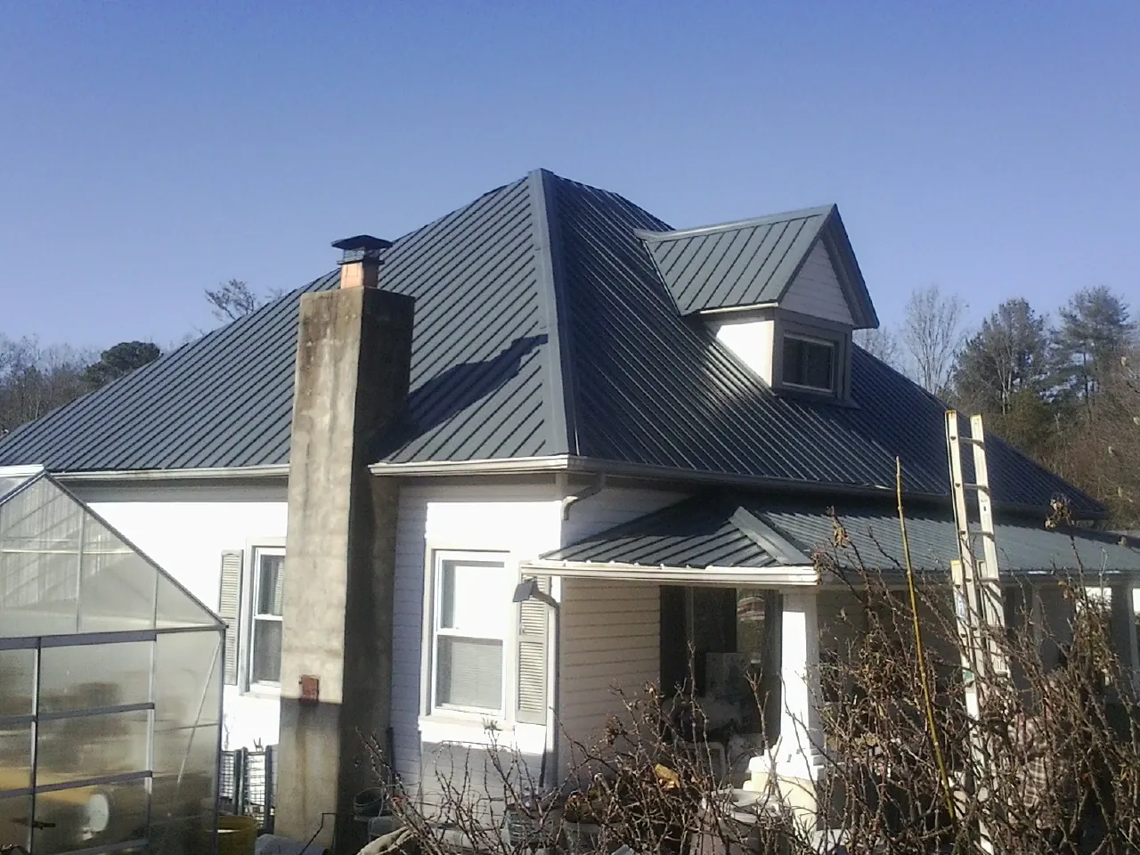 Dark blue standing seam metal roof on a white farmhouse with dormer — Slate & Tile Roof Repair by Roofing Brothers in Mc Clure