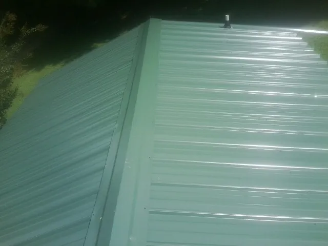 New green metal panels meeting at the ridge of a roof — Flat Roof Repair work by our crew in Mc Clure