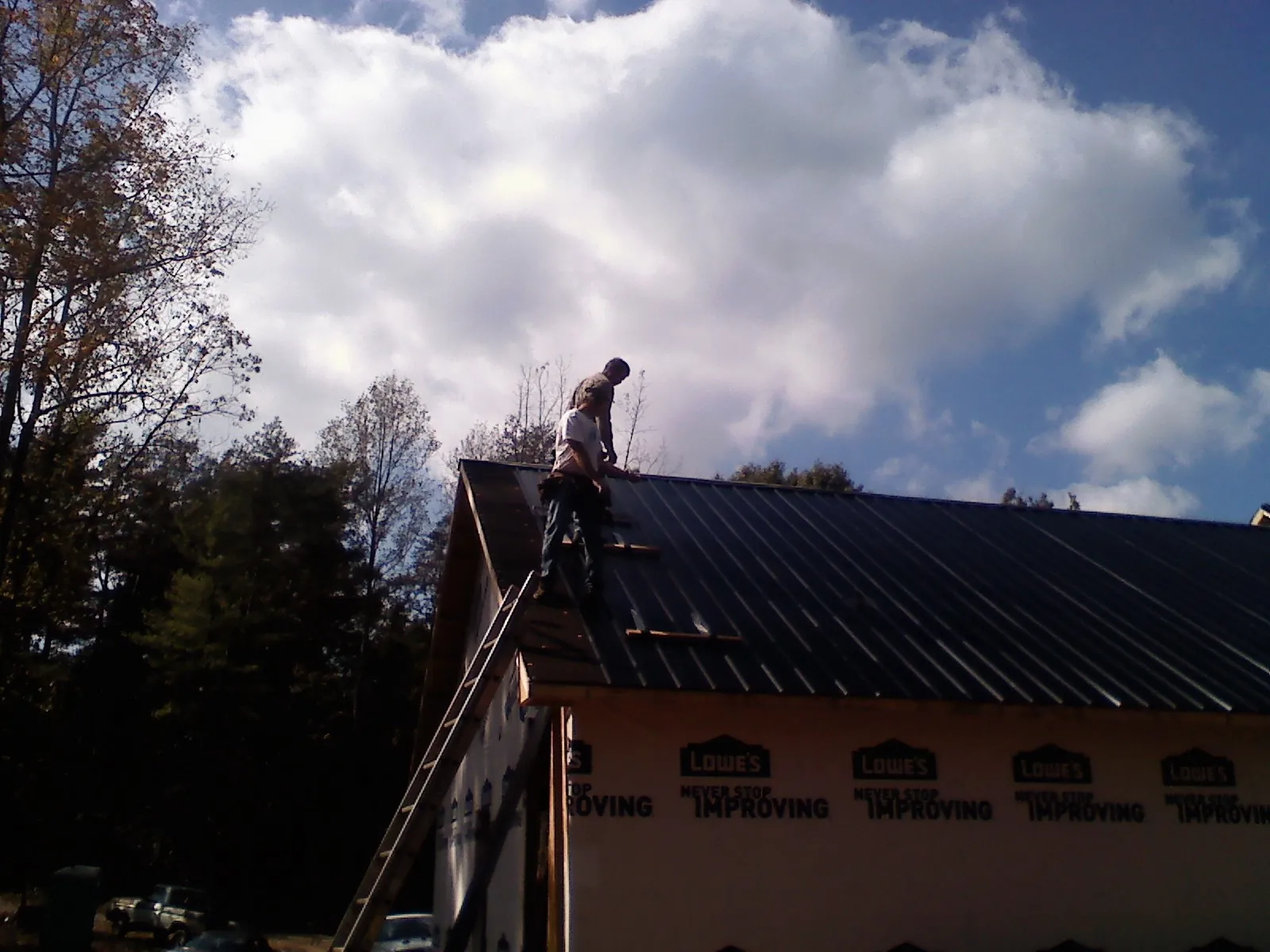 Roofer fastening dark metal panels high against a cloudy sky, from a Roof Inspection job in Mc Clure