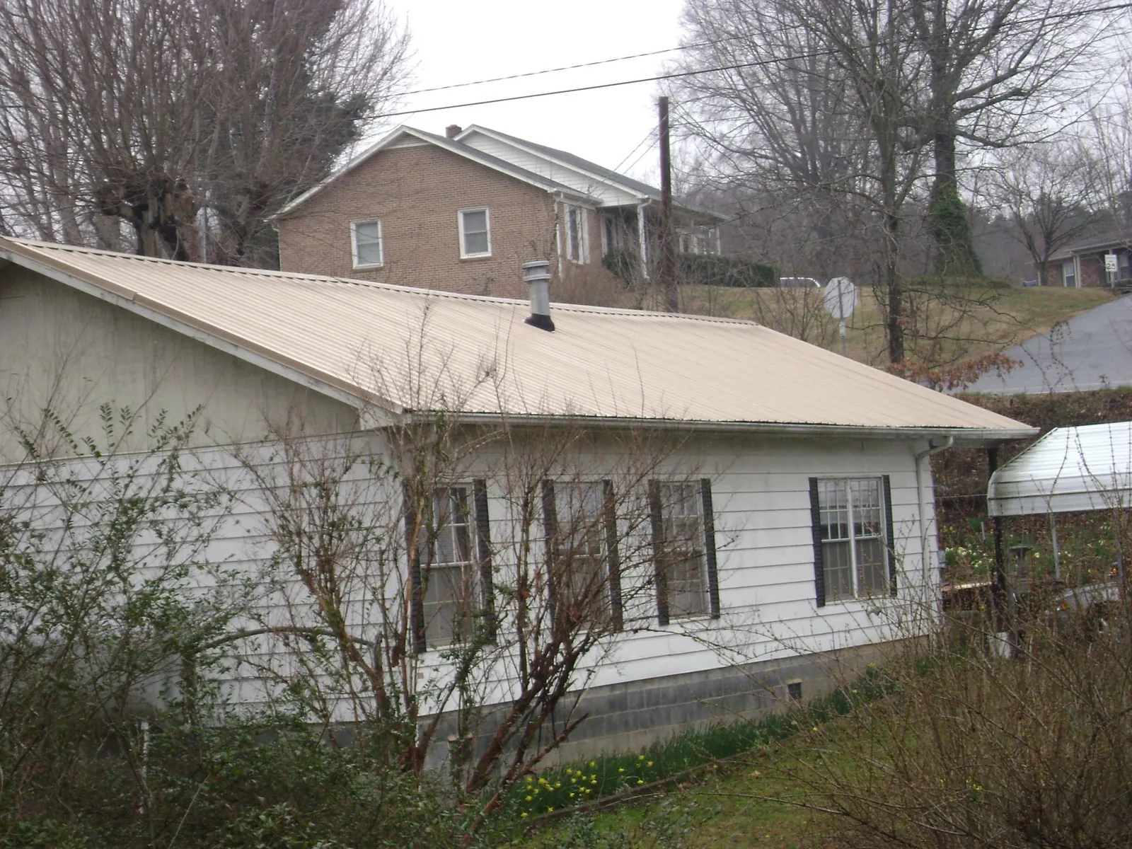Tan metal roof on a white sided house set into a hillside — Commercial Roofing by Roofing Brothers in Mc Clure